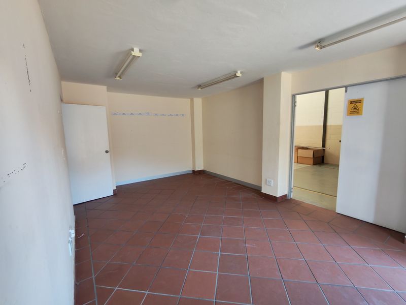 A vacant office space featuring tiled flooring, fluorescent lighting, and direct access to the warehouse area.