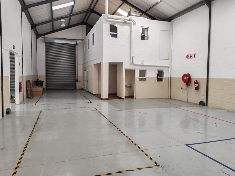 Spacious industrial warehouse unit featuring a high-clearance roller shutter door, mezzanine level, epoxy flooring, and integrated fire safety equipment.