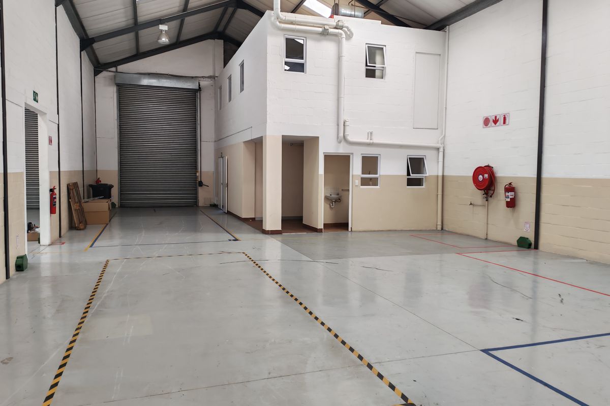 Spacious industrial warehouse unit featuring a high-clearance roller shutter door, mezzanine level, epoxy flooring, and integrated fire safety equipment.