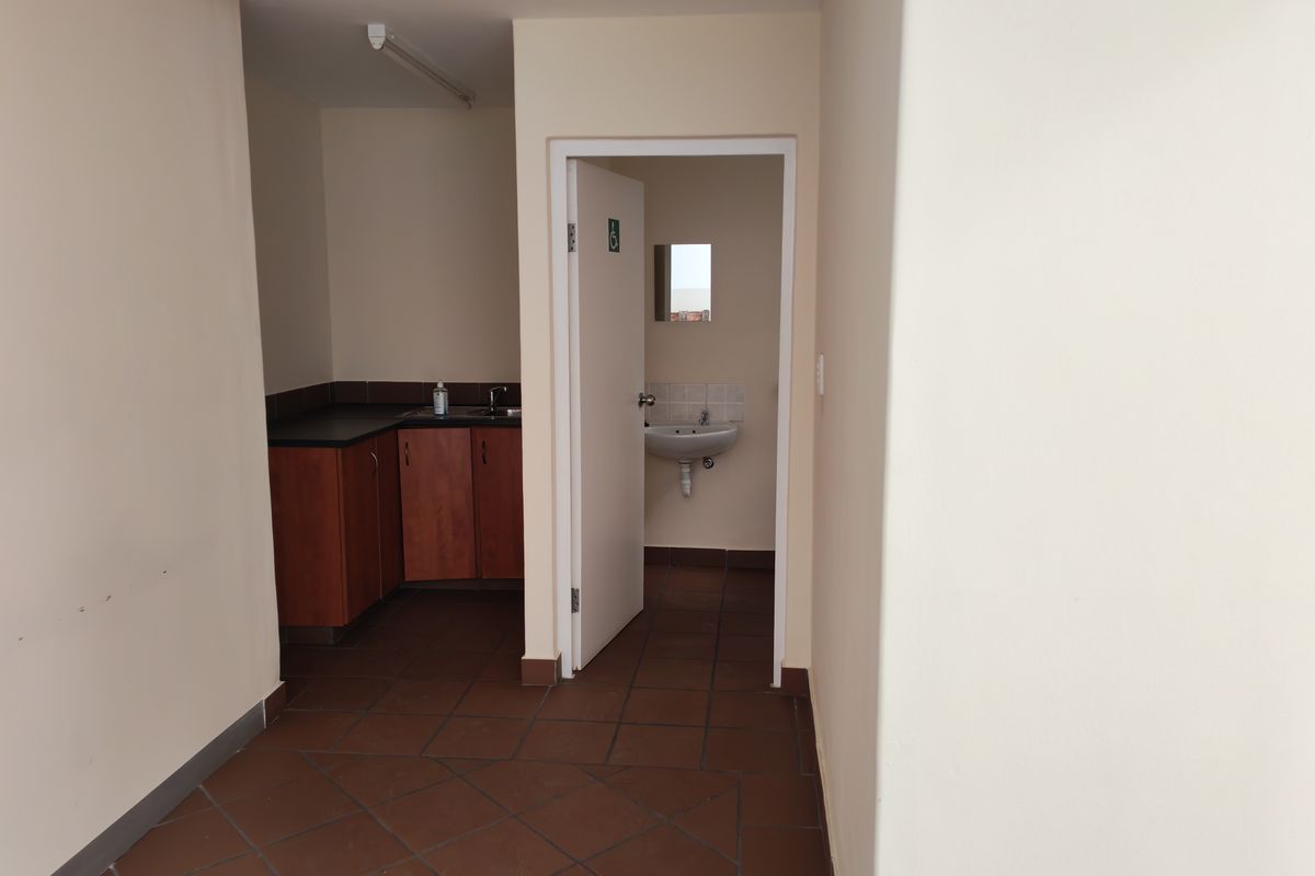A functional industrial kitchenette area featuring built-in cabinetry and a sink, with an adjacent small washroom containing a wall-mounted basin.