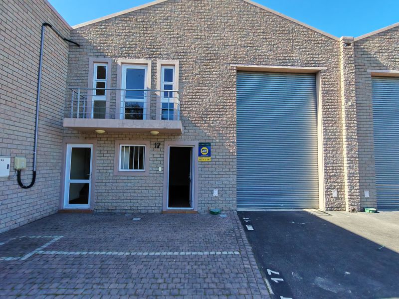 Front elevation of an industrial unit featuring a large roller shutter door, a small balcony, and paved driveway access.