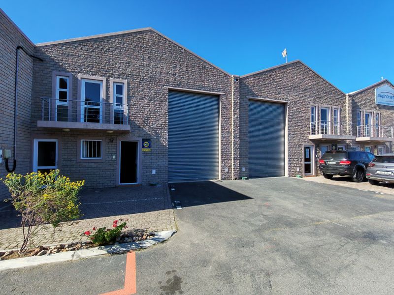 Front elevation of an industrial property featuring stone cladding, large roller shutter doors, and upper-level balconies with paved driveway access.