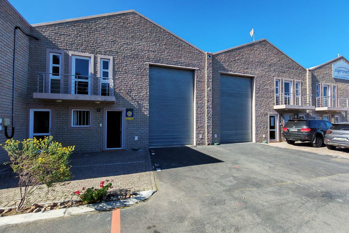 Front elevation of an industrial property featuring stone cladding, large roller shutter doors, and upper-level balconies with paved driveway access.
