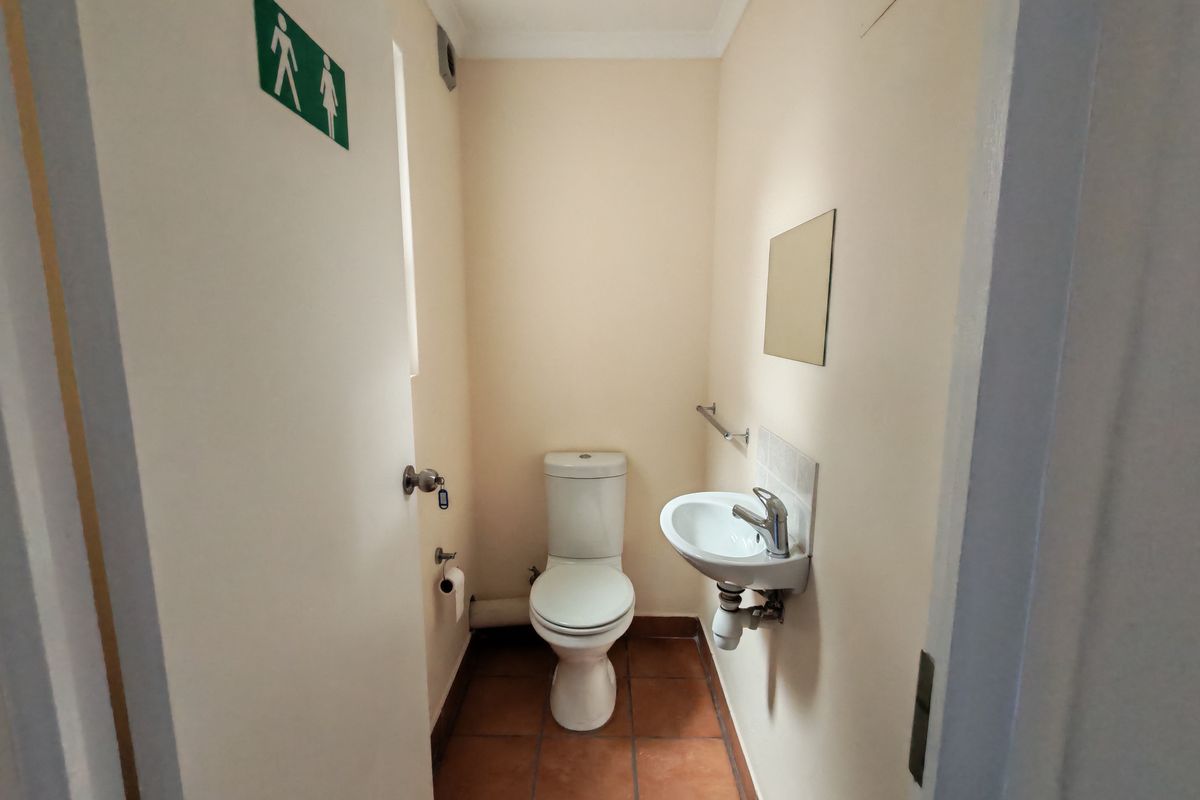 A compact industrial-style restroom featuring a wall-mounted basin, toilet, and tiled flooring, providing essential facilities for the workspace.