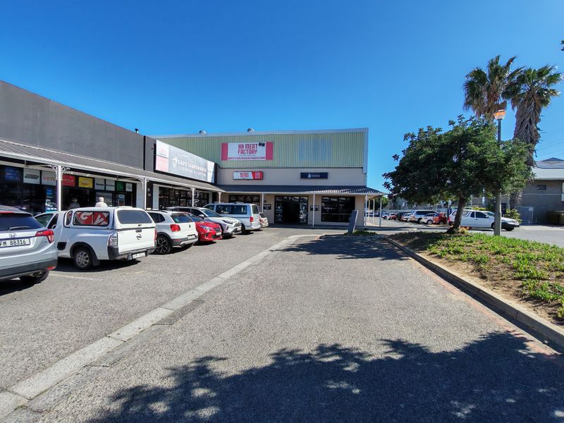 Front exterior view of a commercial industrial complex featuring multiple storefronts, signage, and an asphalt parking area.