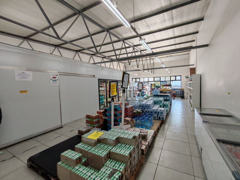 Industrial retail space featuring exposed steel roof trusses, tiled flooring, integrated cold storage units, and commercial refrigeration equipment.