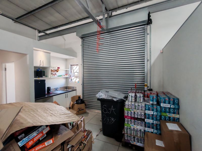 Industrial utility space featuring a large roller shutter door, kitchenette area with sink and cabinetry, and exposed steel roof structure.