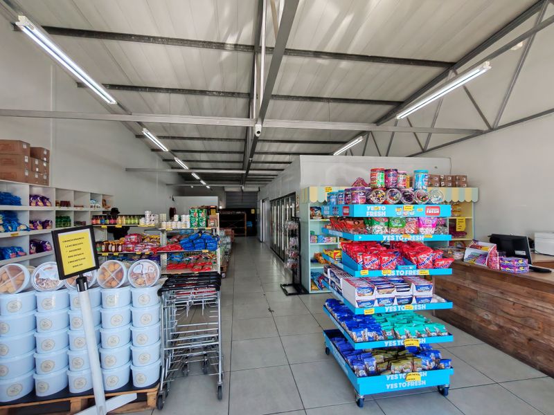 A well-lit industrial retail space featuring exposed steel roof trusses, tiled flooring, and built-in shelving units suitable for commercial operations.
