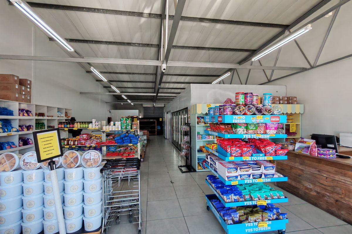 A well-lit industrial retail space featuring exposed steel roof trusses, tiled flooring, and built-in shelving units suitable for commercial operations.