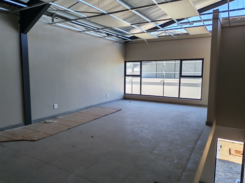 An unfinished industrial office space featuring tiled flooring, large aluminium windows, and an exposed ceiling grid awaiting final installation.