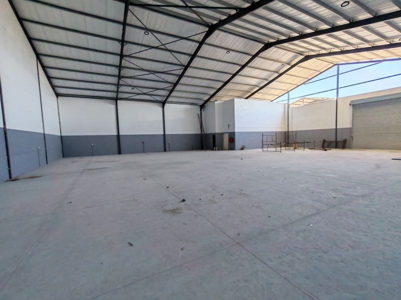 Spacious industrial warehouse unit featuring high ceilings with exposed steel trusses, concrete flooring, and a large roller shutter door for easy access.