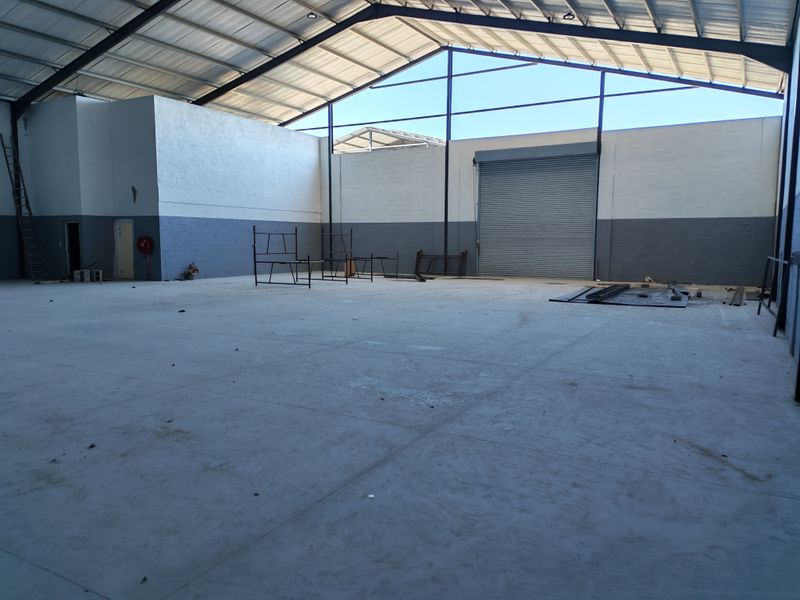 Spacious industrial warehouse unit featuring high ceilings with exposed steel trusses, concrete flooring, and a large roller shutter door for easy access.