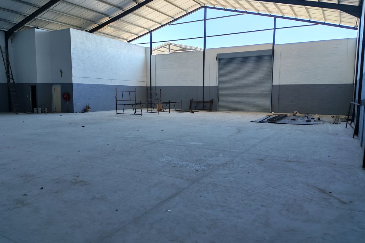 Spacious industrial warehouse unit featuring high ceilings with exposed steel trusses, concrete flooring, and a large roller shutter door for easy access.