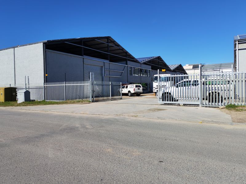 Industrial property featuring multiple warehouse units with roller shutter doors, secure palisade fencing, electric security, and roof-mounted solar panels.