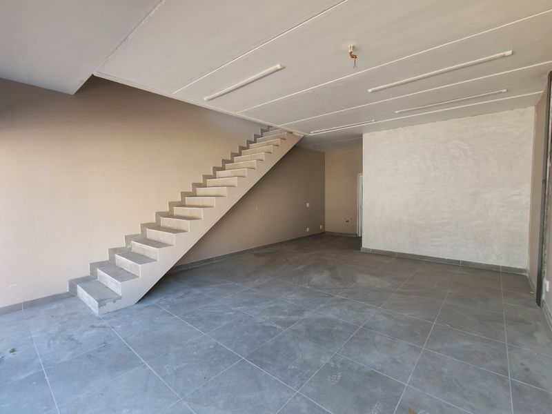 An open-plan industrial space featuring tiled flooring and a concrete staircase, currently in an unfinished state with exposed ceiling wiring.