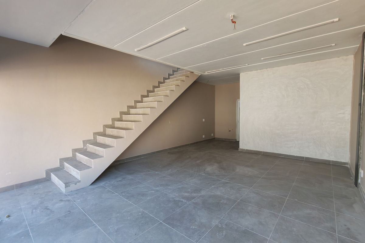 An open-plan industrial space featuring tiled flooring and a concrete staircase, currently in an unfinished state with exposed ceiling wiring.