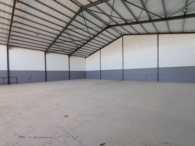 Spacious industrial warehouse unit featuring high-clearance steel truss roofing, durable concrete flooring, and clean painted masonry walls, suitable for various commercial or storage uses.