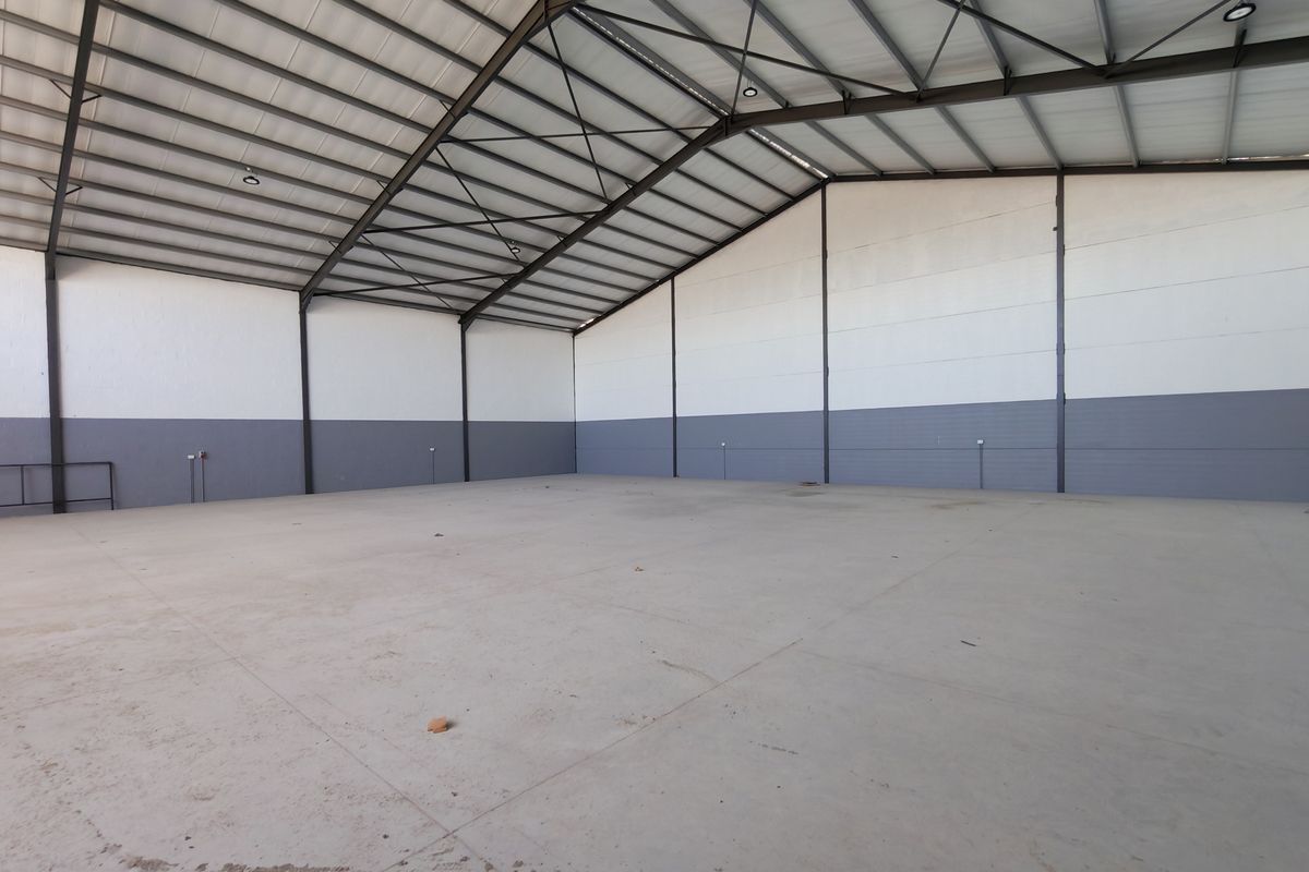 Spacious industrial warehouse unit featuring high-clearance steel truss roofing, durable concrete flooring, and clean painted masonry walls, suitable for various commercial or storage uses.