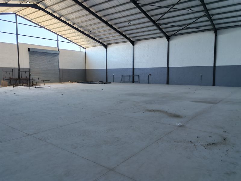 Spacious industrial warehouse unit featuring high ceilings, exposed steel portal frame, concrete flooring, and a large roller shutter door for easy access.