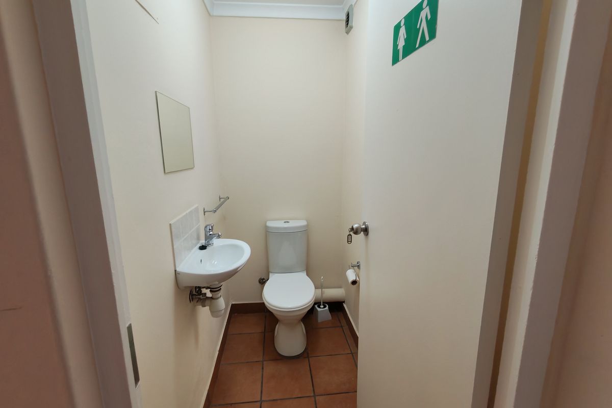 A functional, compact industrial restroom featuring a wall-mounted basin, toilet, and tiled flooring, suitable for office or warehouse use.