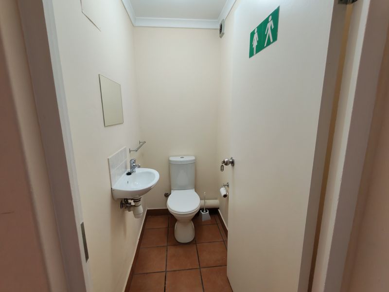 A functional, compact industrial restroom featuring a wall-mounted basin, toilet, and tiled flooring, suitable for office or warehouse use.