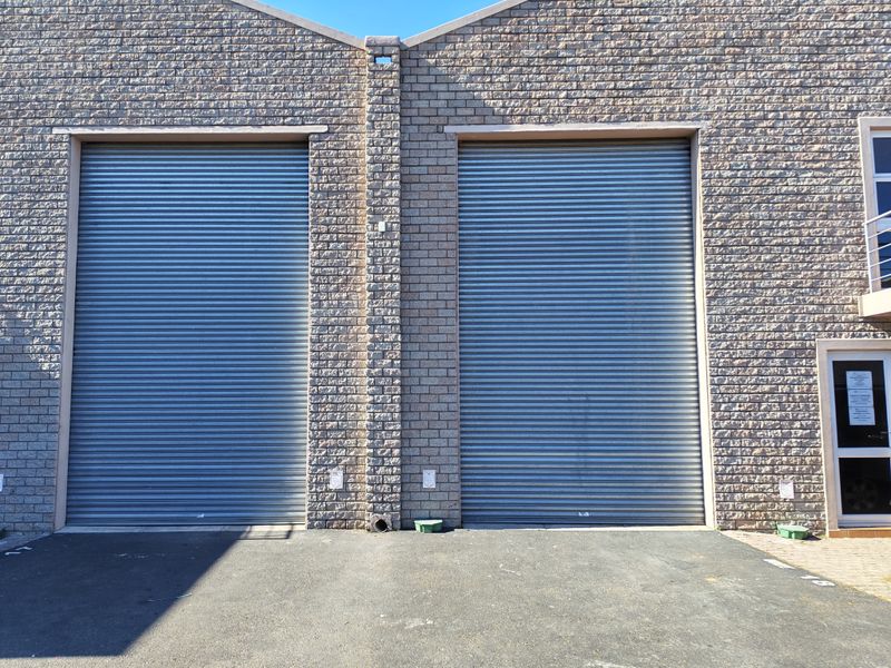 Industrial property exterior featuring two large roller shutter doors and a durable face brick facade with an asphalt driveway.