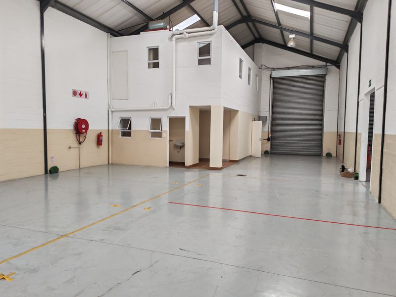 Spacious industrial warehouse unit featuring high ceilings with exposed steel trusses, a large roller shutter door, and an integrated mezzanine office area.
