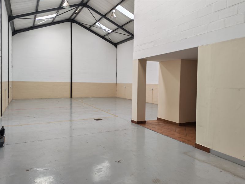 Spacious industrial open-plan unit featuring high ceilings with exposed steel trusses, skylights, durable epoxy flooring, and a dedicated tiled entrance area.