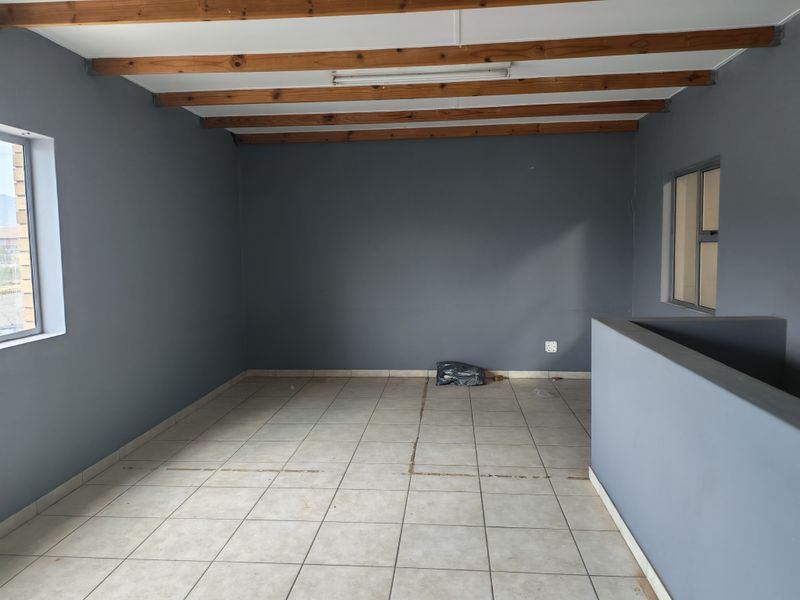 An open-plan industrial space featuring exposed timber ceiling beams, ceramic tiled flooring, and neutral grey walls, offering a versatile layout for various business uses.