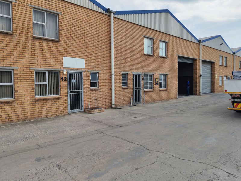 Industrial unit exterior featuring face brick facade, roller shutter doors, and secure access points with a concrete driveway.