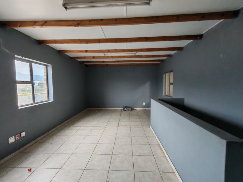 An open-plan office space featuring exposed timber ceiling beams, tiled flooring, and a half-height partition wall, offering a versatile industrial workspace.
