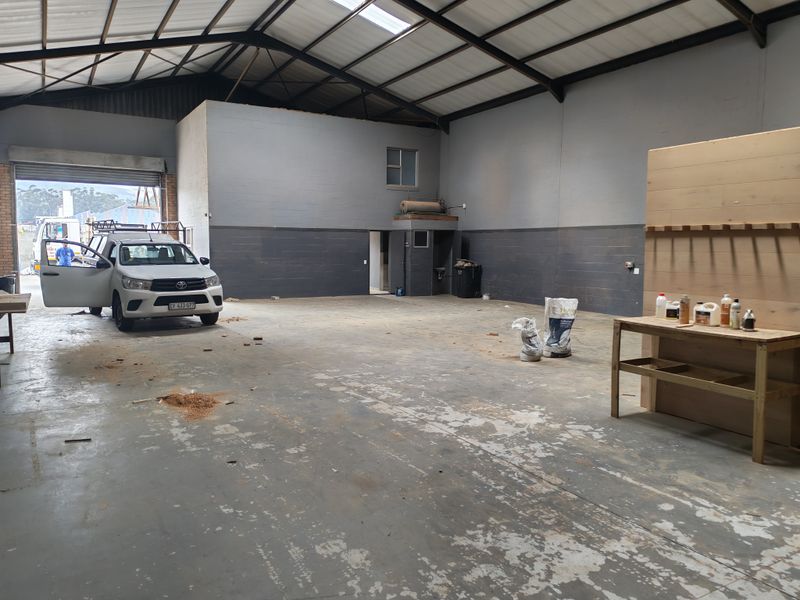 Spacious industrial garage or workshop area featuring high ceilings with exposed steel trusses, concrete flooring, and a large roller shutter door for vehicle access.
