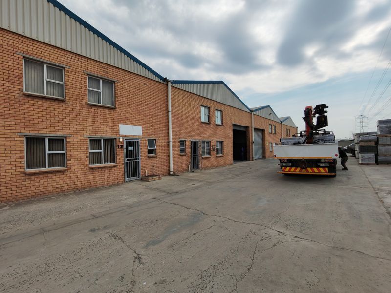 Industrial warehouse exterior featuring face brick facade, multiple access points, roller shutter doors, and a paved concrete yard area.
