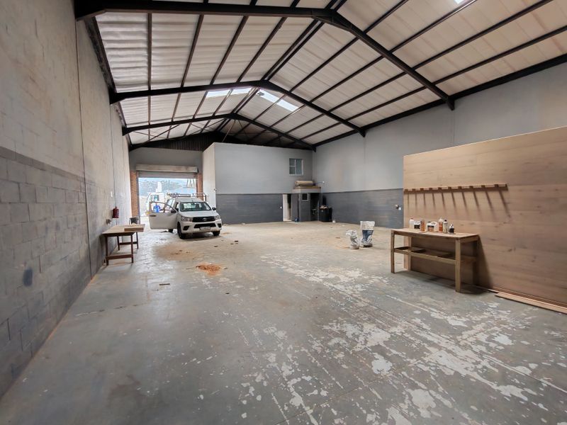 Spacious industrial utility area featuring high ceilings with exposed steel trusses, concrete flooring, and natural light from skylights, suitable for workshop or storage use.