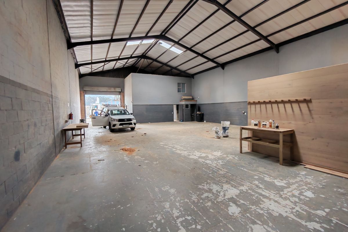 Spacious industrial utility area featuring high ceilings with exposed steel trusses, concrete flooring, and natural light from skylights, suitable for workshop or storage use.