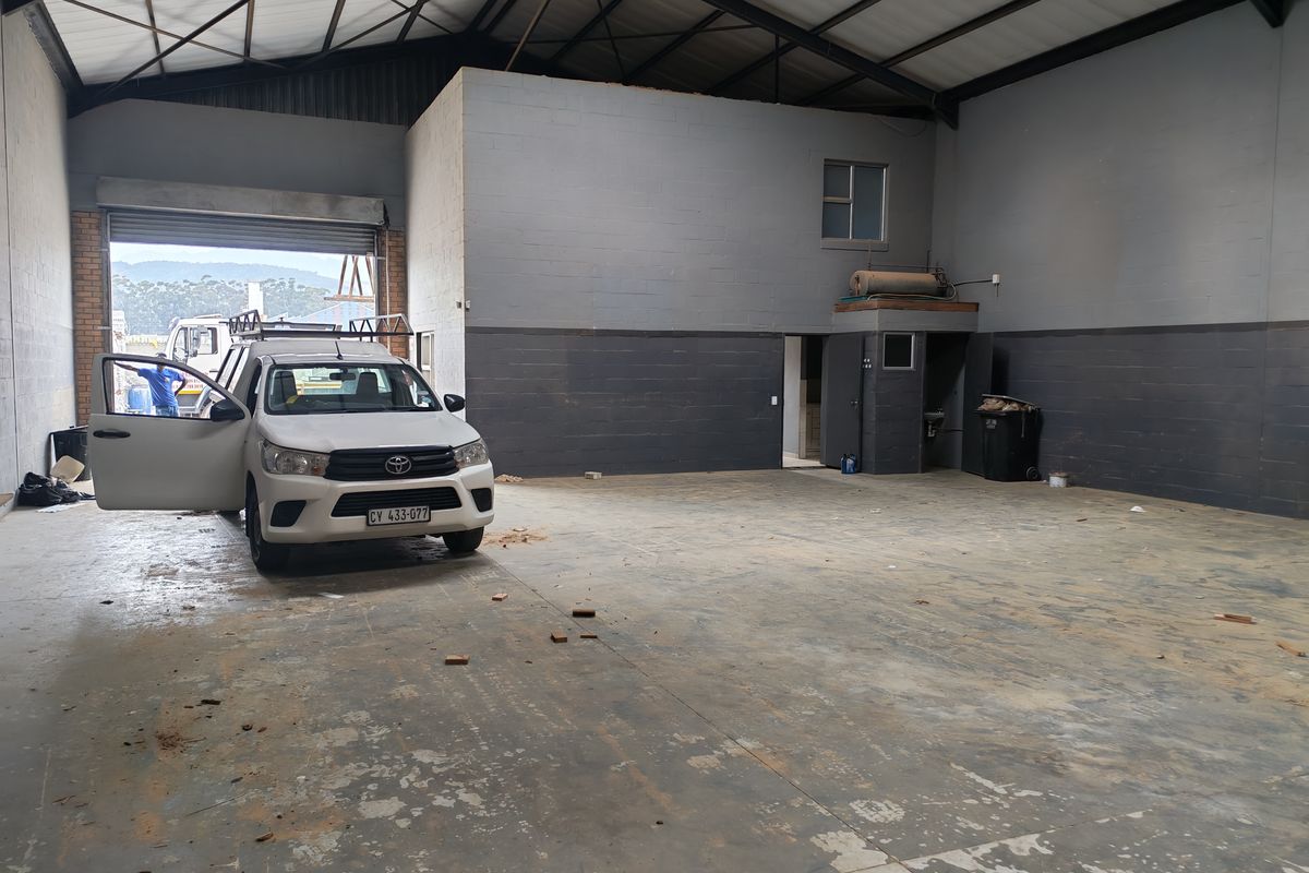 Spacious industrial warehouse unit featuring high ceilings with exposed steel trusses, concrete flooring, and a large roller shutter door for vehicle access.