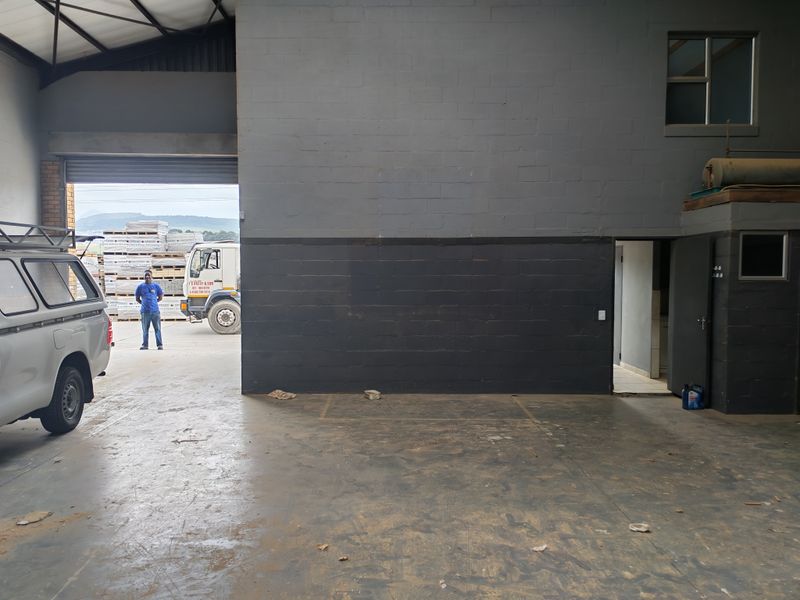 Spacious industrial garage area featuring high ceilings with exposed steel trusses, durable concrete flooring, and direct access through a large roller shutter door.