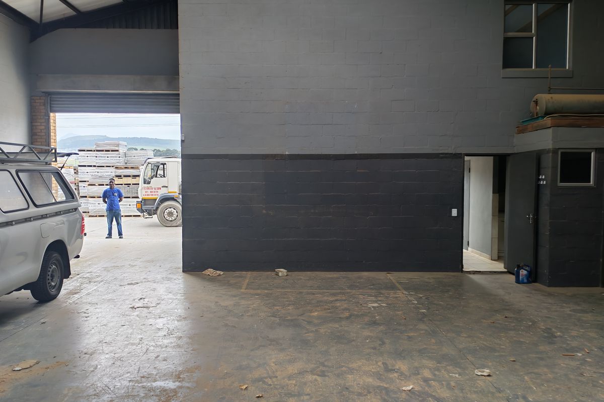 Spacious industrial garage area featuring high ceilings with exposed steel trusses, durable concrete flooring, and direct access through a large roller shutter door.