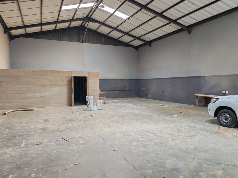 Spacious industrial utility area featuring high ceilings with exposed steel trusses, skylights, concrete flooring, and a timber-clad partition wall.