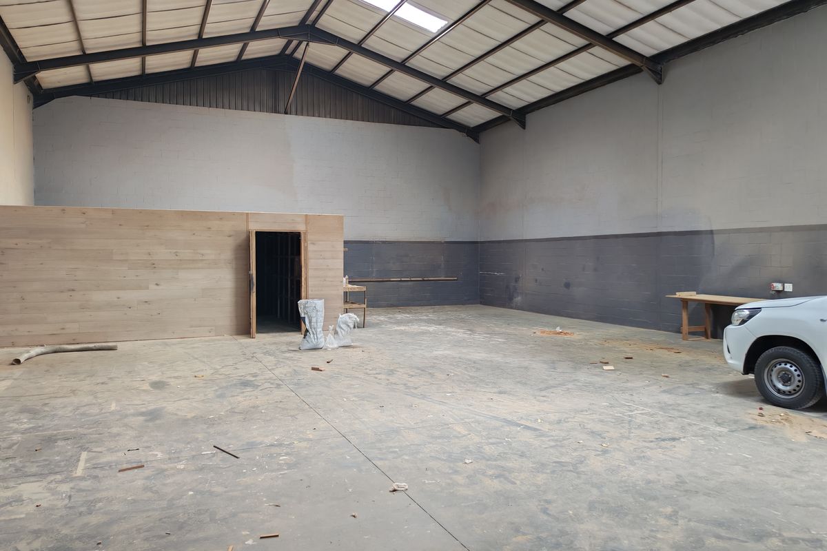 Spacious industrial utility area featuring high ceilings with exposed steel trusses, skylights, concrete flooring, and a timber-clad partition wall.