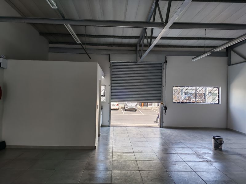 Spacious industrial utility space featuring tiled flooring, exposed steel roof trusses, and a large roller shutter door for easy access.