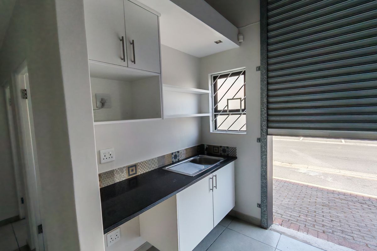 Compact industrial kitchen area featuring built-in cabinetry, a stainless steel sink, black granite countertops, and direct access via a roller shutter door.