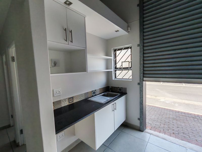 Compact industrial kitchen area featuring built-in cabinetry, a stainless steel sink, black granite countertops, and direct access via a roller shutter door.