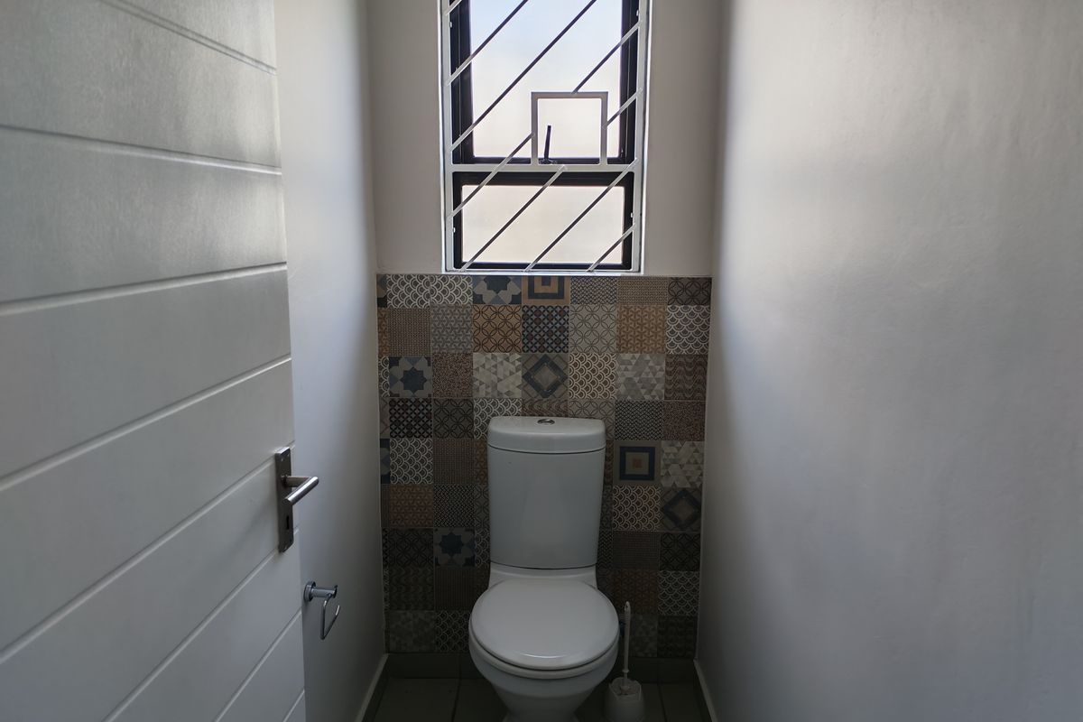 A clean and compact guest bathroom featuring modern patterned wall tiles, a white toilet, and a window with security bars.