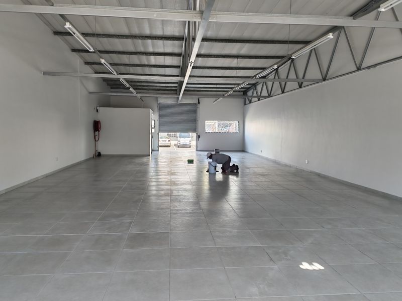 Spacious industrial unit featuring tiled flooring, exposed steel roof trusses, and a roller shutter door, suitable for various commercial or storage applications.