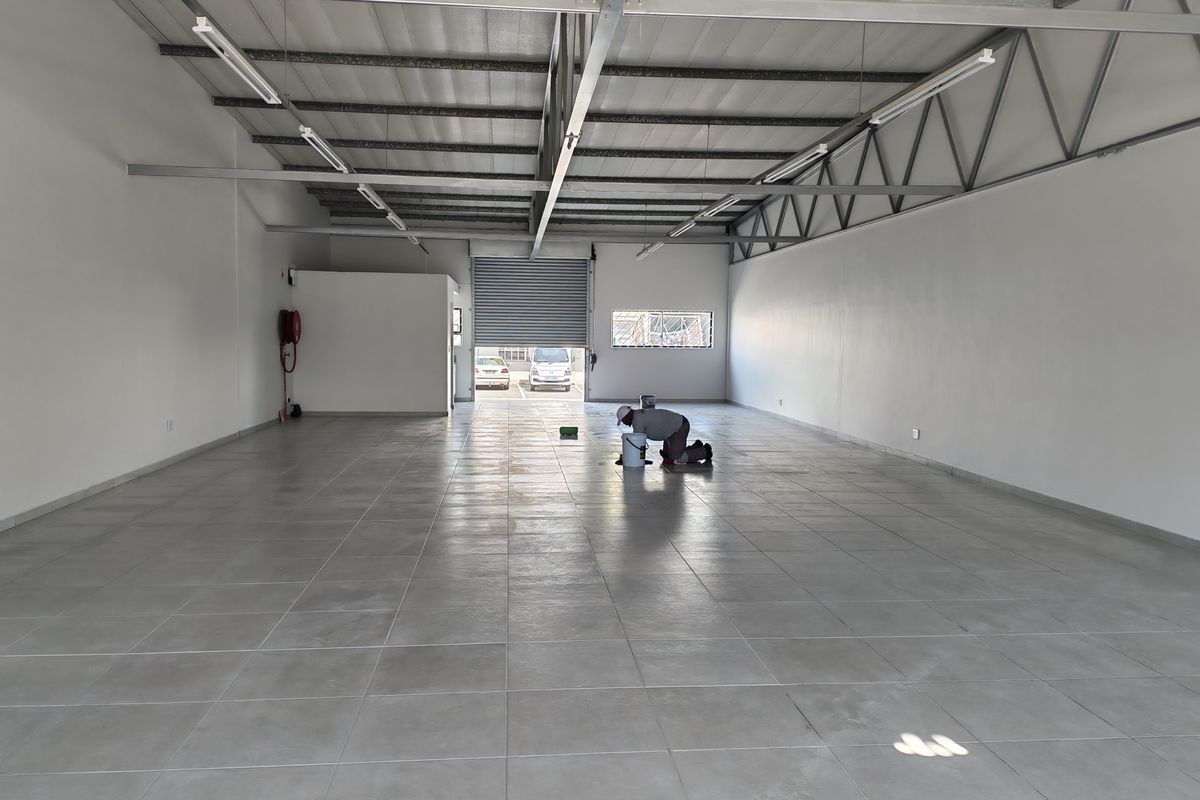 Spacious industrial unit featuring tiled flooring, exposed steel roof trusses, and a roller shutter door, suitable for various commercial or storage applications.