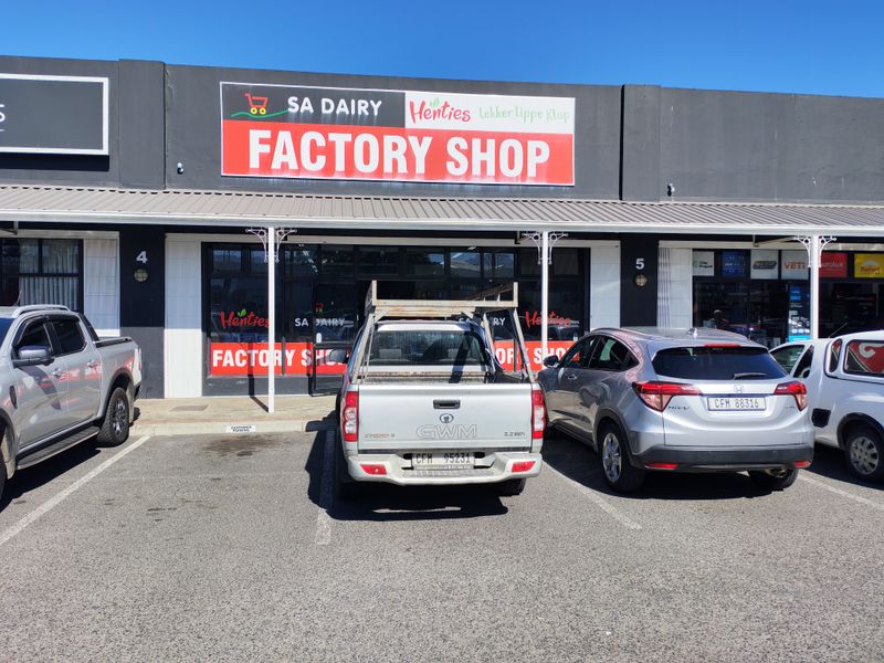 Front exterior view of an industrial factory shop unit featuring a glass storefront, metal awning, and dedicated parking space.