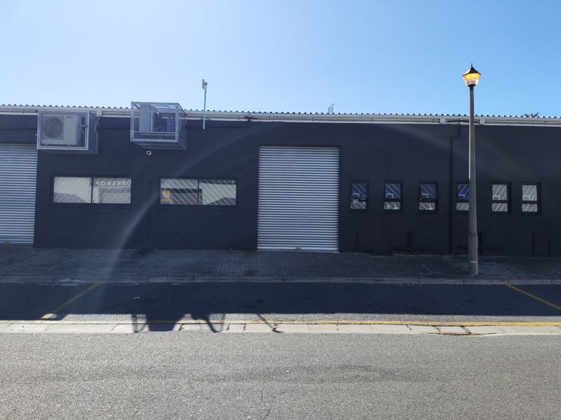 Industrial street-facing facade featuring roller shutter doors, security-caged air conditioning units, and modern dark exterior paint finish.