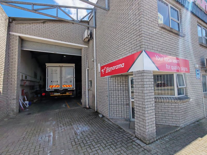 Industrial property exterior featuring a large roller shutter door for vehicle access, brick facade, and prominent signage above the entrance.