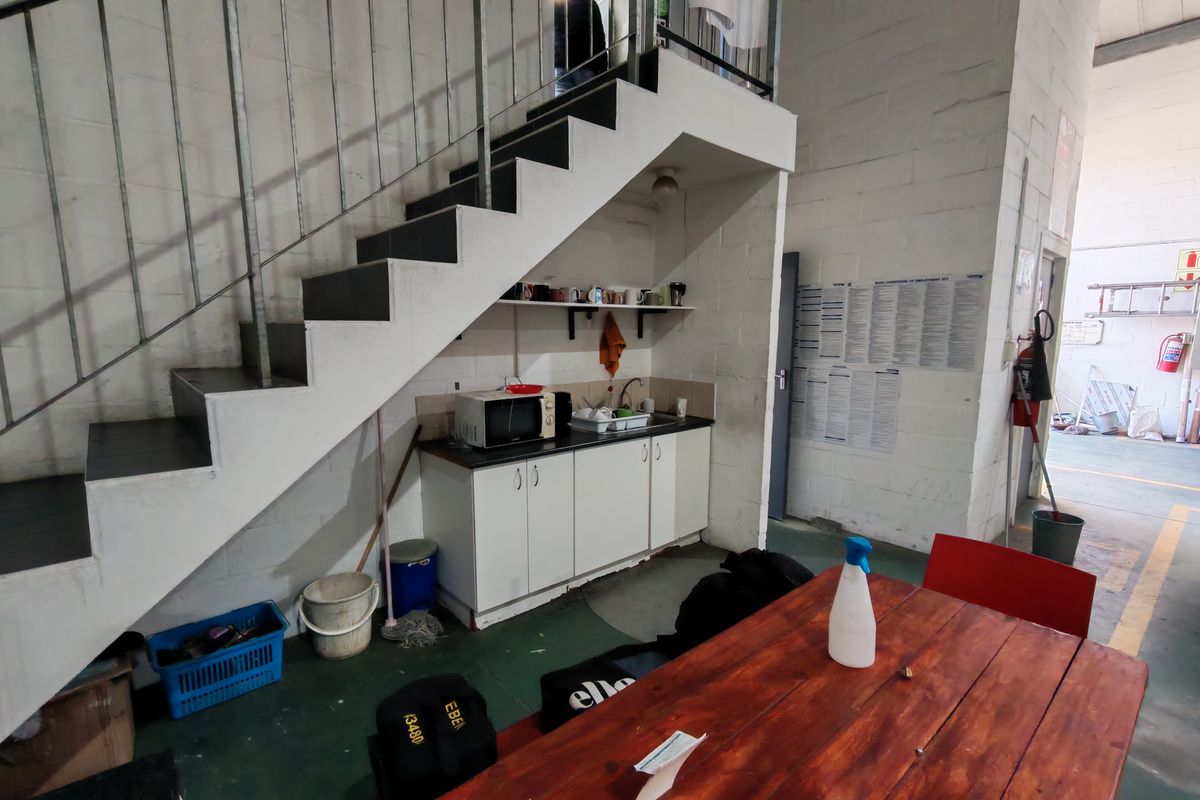 A compact kitchenette area located beneath a staircase, featuring built-in cabinetry, a sink, and industrial-style exposed blockwork walls.